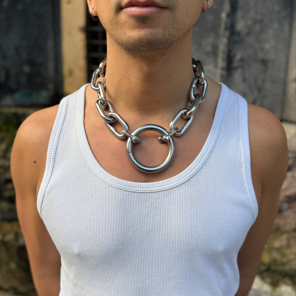 Man wearing a white tank top and large chain necklace against a blurred background