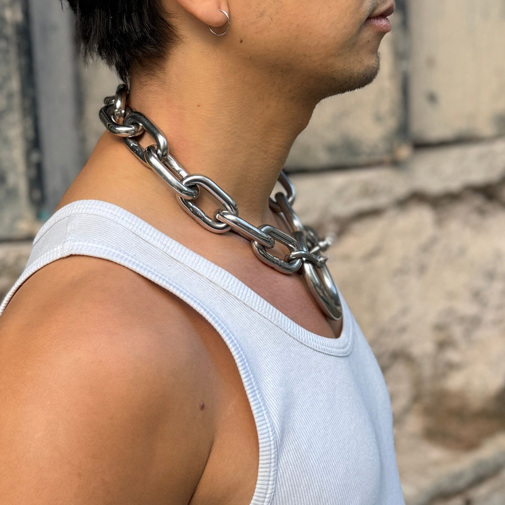 Person wearing a white tank top and chain necklace against a textured wall.